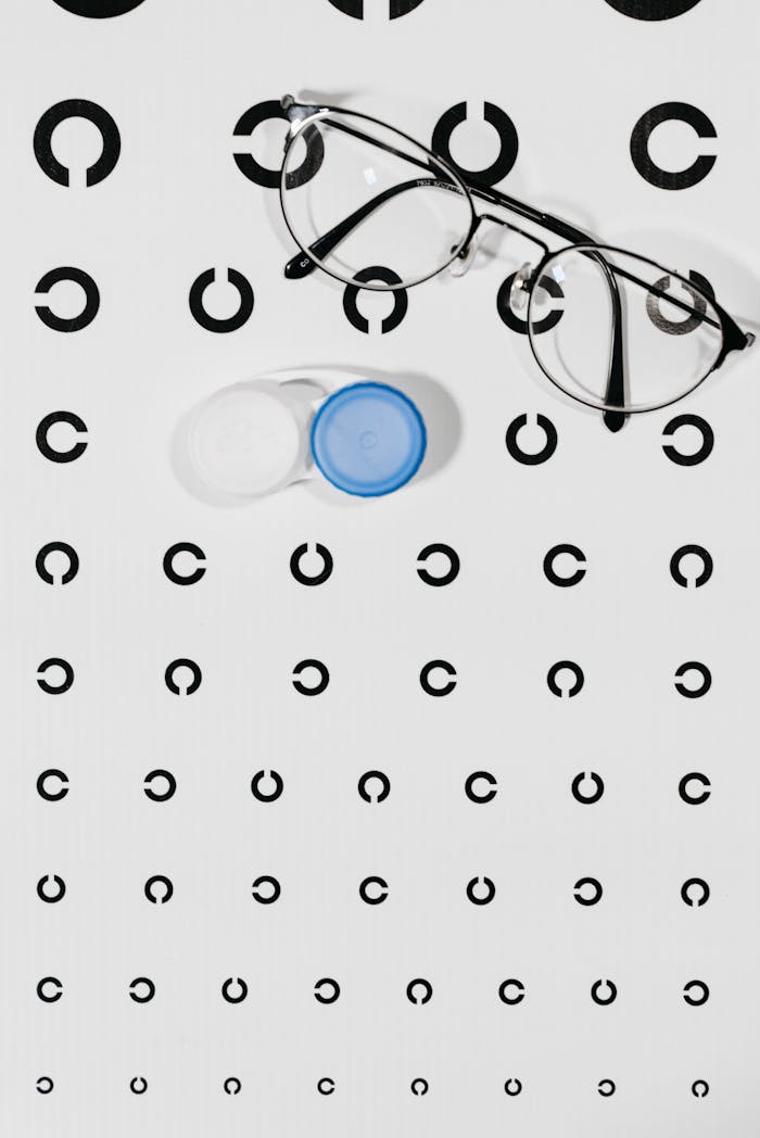 High angle view of eyeglasses and contact lens case on an eye test chart, emphasizing vision care.